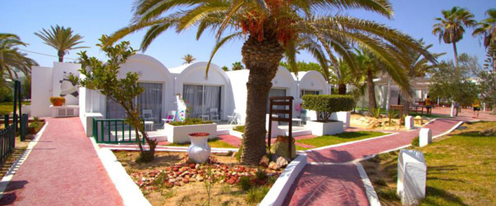 Im weitläufigen Resort des Hotel Meninx prägen Palmen und typische mediterrane Vegetation die Anlage, während ein klarer Sommertag für helle, ruhige Atmosphäre sorgt.
